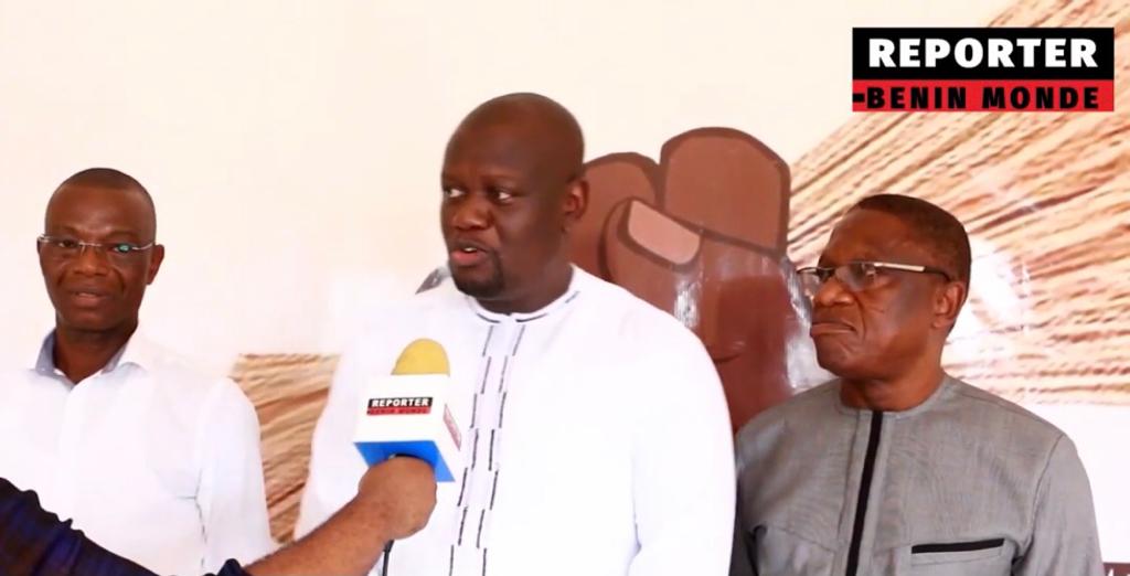 Trois hommes en train de répondre à une interview devant un mur décoré avec un logo Reporter Benin Monde