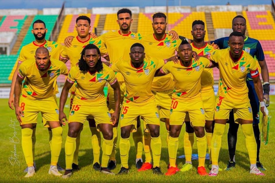 Onze joueurs de football en tenue jaune posent en rangée sur un terrain face à la caméra dans un stade presque vide