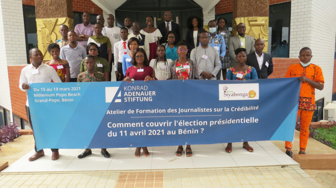 Groupe de personnes posant devant un bâtiment avec une grande bannière bleue sur la couverture d'une élection présidentielle