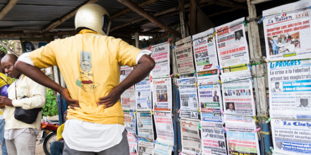 Un homme en casque observe des unes de journaux affichés sur un mur dans un kiosque extérieur