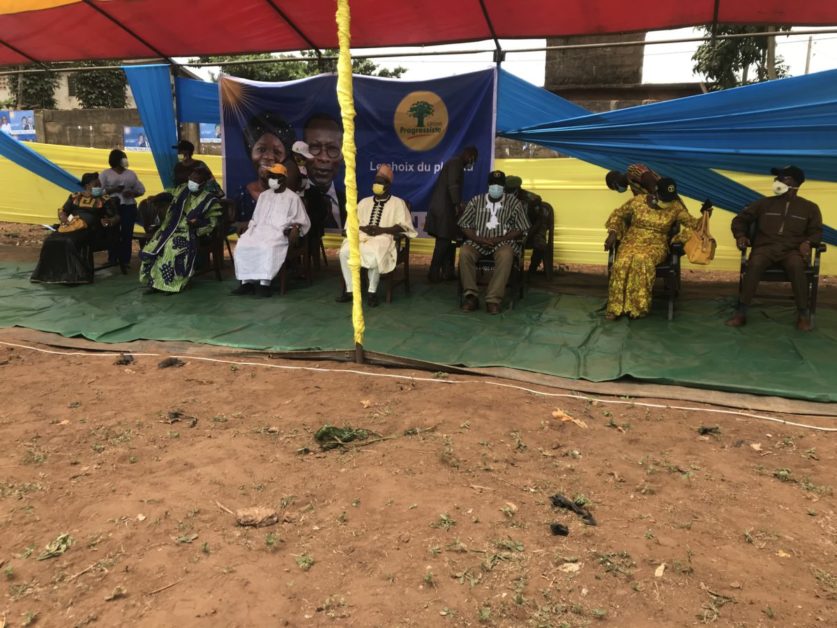 Groupe de personnes assises sous une tente avec une banderole bleue affichant un logo et du texte partiellement lisible