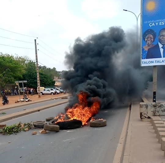 Pneus en feu au milieu d'une route déserte avec de la fumée noire et un panneau publicitaire visible sur le côté