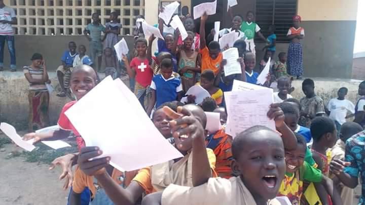 Des enfants rassemblés devant un bâtiment agitent des feuilles en souriant et manifestent de la joie