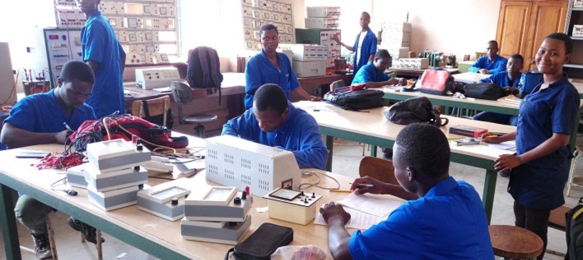 Des élèves en tenue bleue travaillent sur des appareils électriques dans un atelier technique d’école