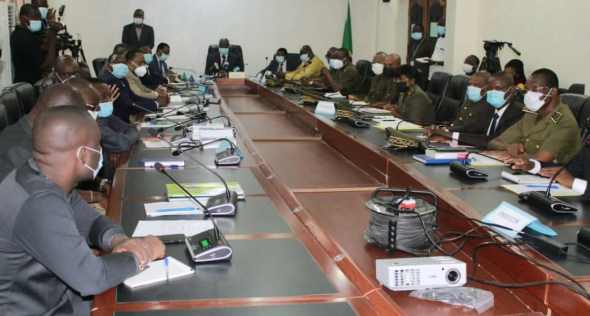 Personnes masquées assises autour d'une grande table de réunion dans une salle avec équipements audio et vidéos