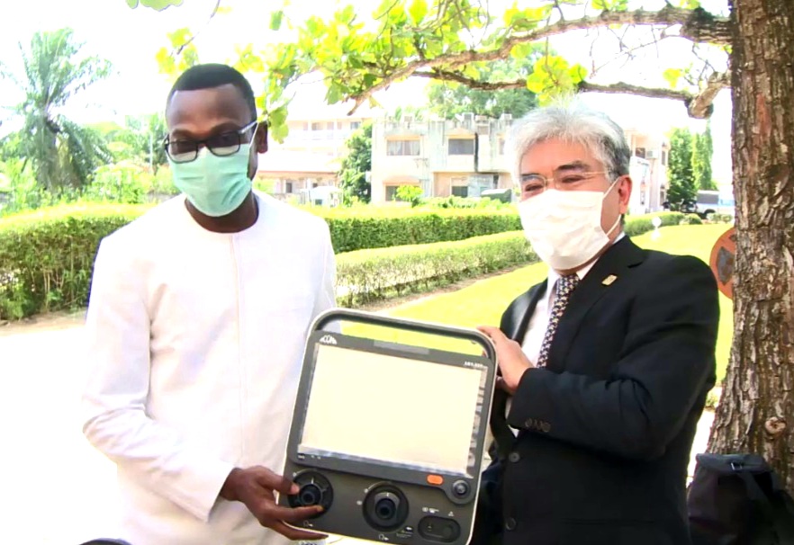 Deux hommes masqués échangent un appareil médical électronique sous un arbre dans un jardin urbain
