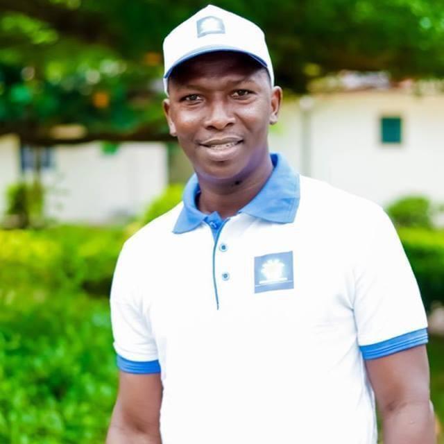 Homme souriant en polo blanc et casquette blanche debout devant un jardin flou en arrière-plan
