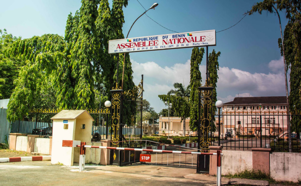 Entrée principale d un bâtiment avec un portail noir orné et une enseigne « Assemblée Nationale » sous un ciel bleu partiellement nuageux