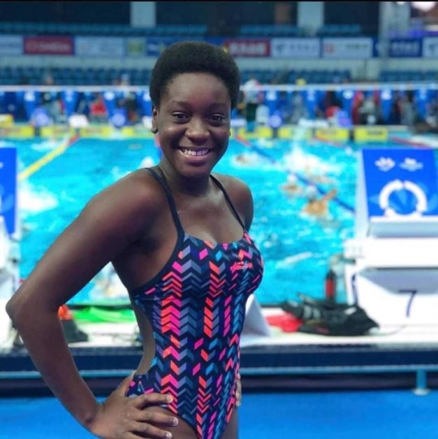 Jeune nageuse souriante en maillot de bain coloré posant devant un bassin de natation en intérieur