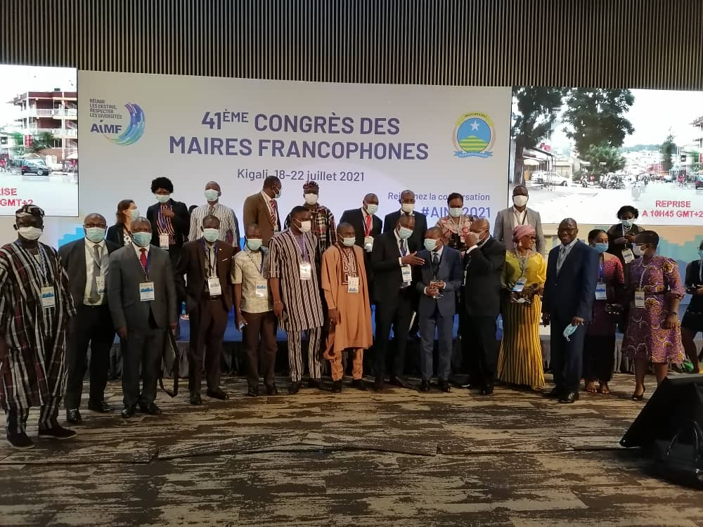 Groupe de personnes posant devant un panneau avec texte «41ème congrès des Maires Francophones» avec masques et badges d’identification