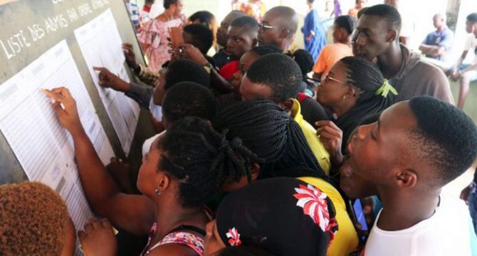 Un groupe de jeunes consultent intensément des listes affichées sur un mur dans un lieu public.