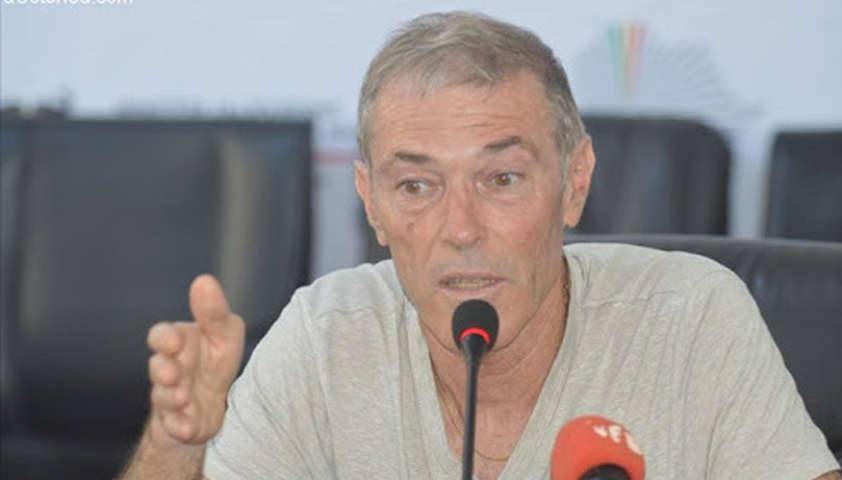 Un homme parle en gesticulant devant un micro rouge lors d’une conférence de presse