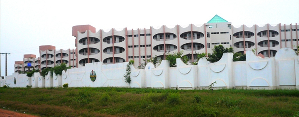 Grand bâtiment moderne derrière un mur blanc orné de motifs et de végétation devant un terrain herbeux