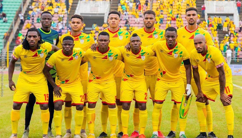 Onze joueurs de football en tenue jaune posent ensemble sur un terrain avec des gradins colorés en arrière-plan