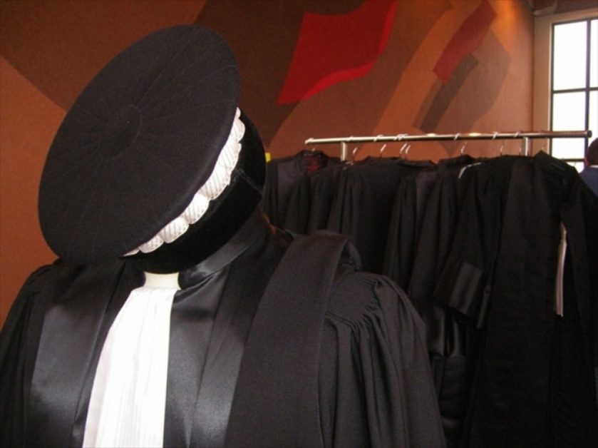 Robe et toque d’auditeur de justice suspendues sur un porte-manteau dans une pièce aux murs peints en rouge et orange