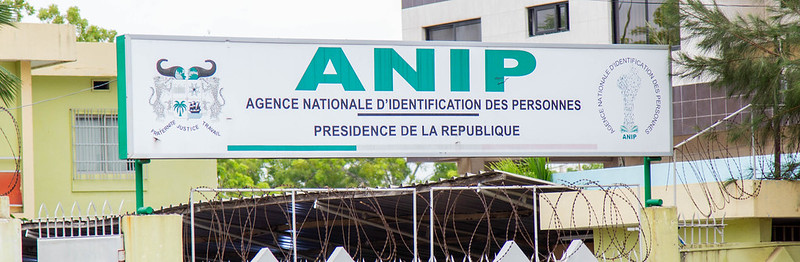 Entrée d'un bâtiment avec un panneau ANIP Agence Nationale d'Identification des Personnes et des grilles avec barbelés devant