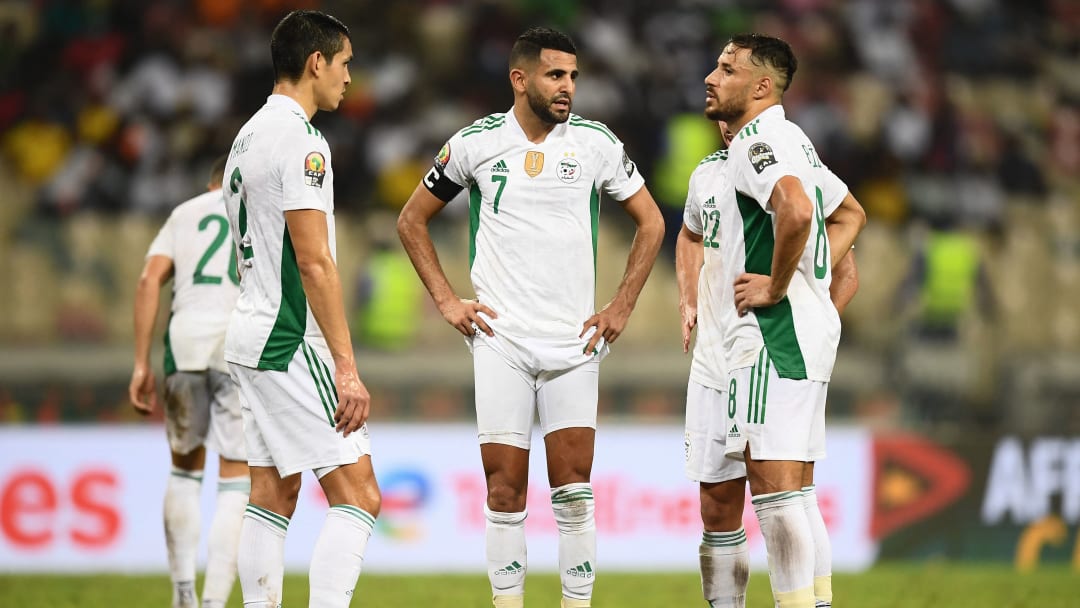 Quatre joueurs de football en tenue blanche avec des détails verts discutent sur le terrain pendant un match