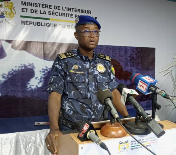 Un officier de police en uniforme bleu marine casque bleu parle devant plusieurs microphones lors d’une conférence de presse