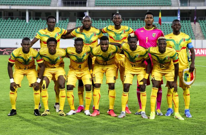 Onze joueurs de football en tenue jaune posant sur un terrain de stade devant des gradins vides