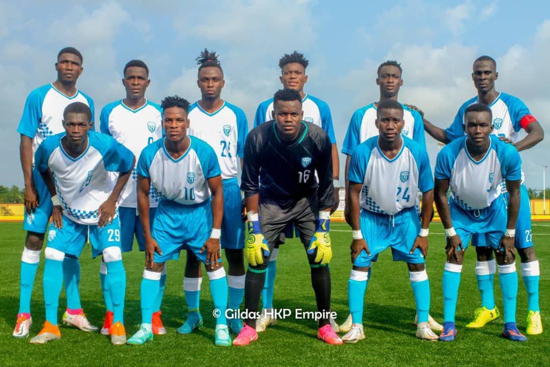 Onze joueurs de football en tenue bleue et blanche posant en formation sur un terrain herbeux sous un ciel partiellement nuageux