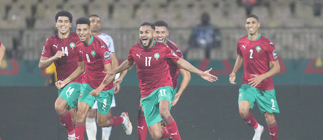 Joueurs en maillots rouges et shorts verts célèbrent un but sur le terrain de football sous les projecteurs
