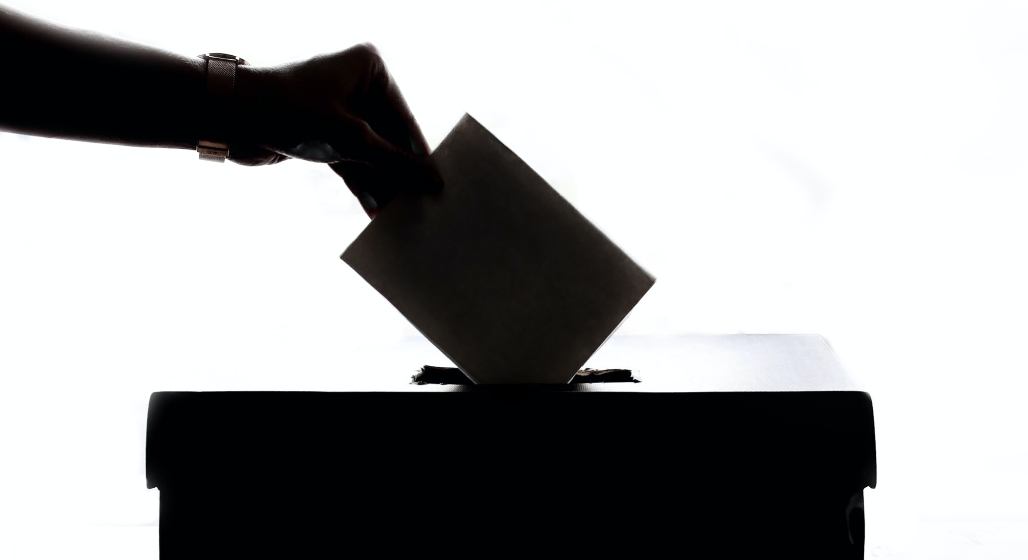 Main déposant un bulletin dans une urne de vote devant un fond blanc lumineux