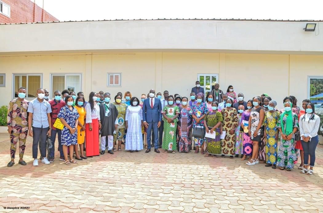 Grand groupe de personnes debout dehors devant un bâtiment blanc, la plupart portant des masques et des vêtements colorés variés