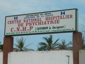 Panneau d’entrée d’un centre national hospitalier de psychiatrie face à un ciel bleu avec trois palmiers derrière un mur blanc