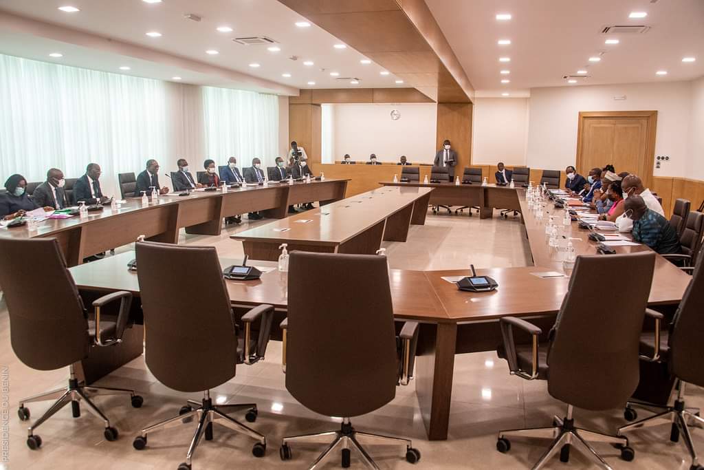 Réunion en salle avec des personnes assises des deux côtés d'une grande table en U discutant d'un sujet formel