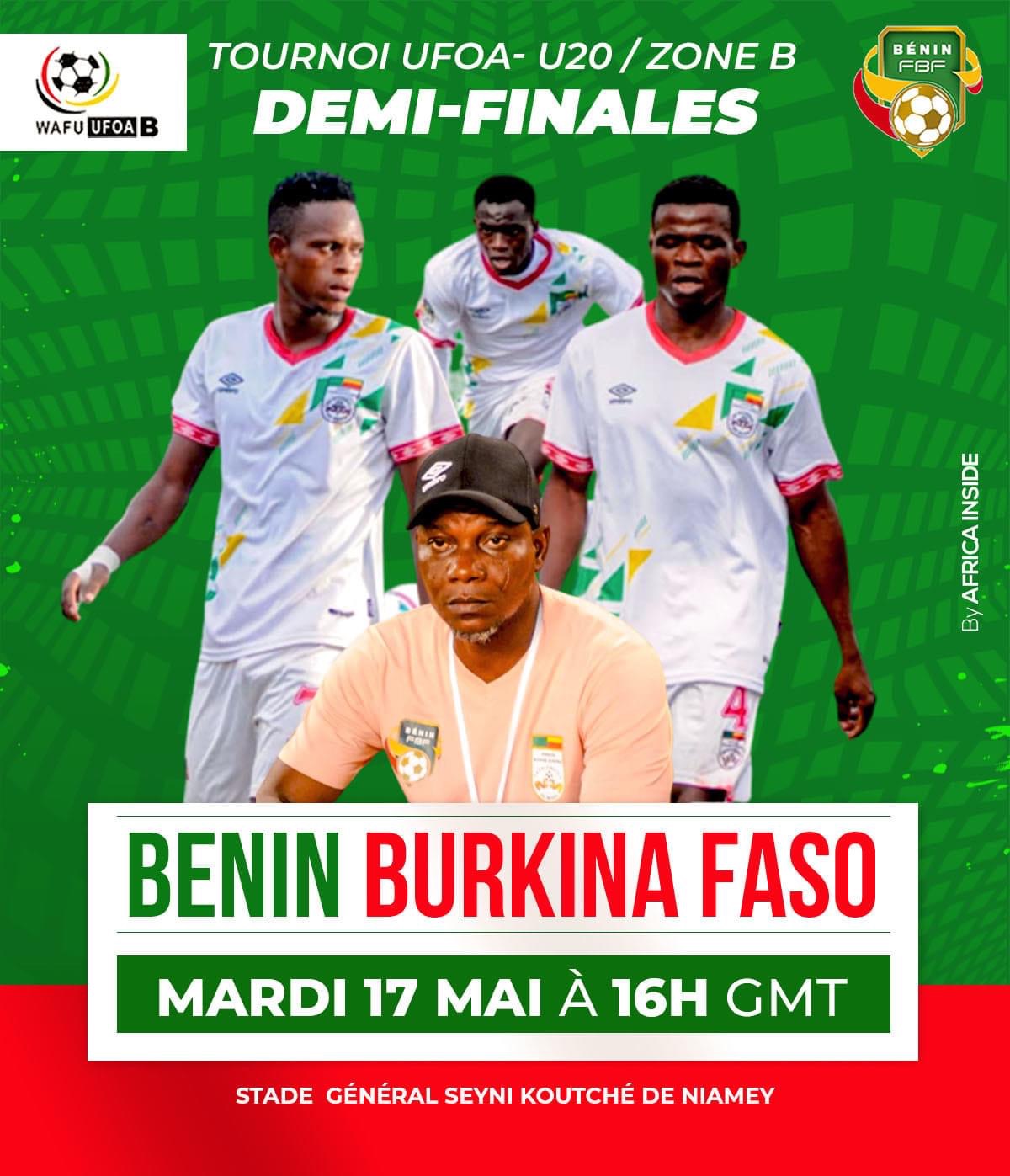 Trois joueurs en maillots blancs avec motifs colorés marchent derrière un homme en t-shirt rose et casquette noire sur fond vert avec texte sur un match de foot