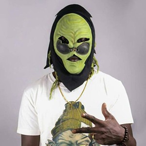 Personne portant un masque vert et des lunettes de soleil, un T-shirt blanc et faisant un geste de la main devant un fond clair