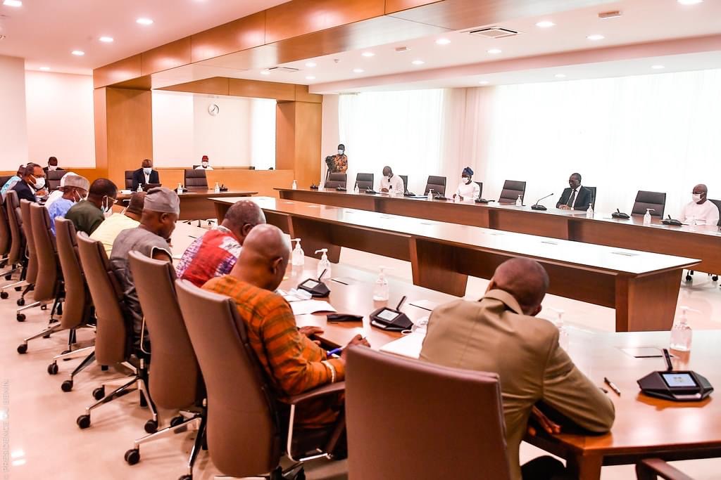 Des personnes assises autour d'une grande table de réunion dans une salle éclairée par des plafonniers et une fenêtre.