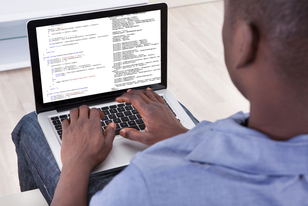 Un homme tape sur un ordinateur portable affichant du code informatique assis sur une chaise.