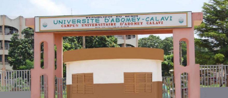 Entrée principale d'une université avec un portail rose et un panneau vert blanc indiquant le nom de l'établissement