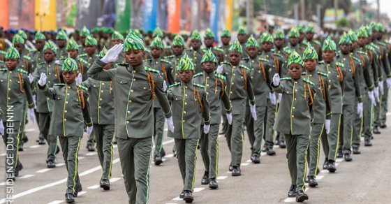 Des jeunes en uniforme militaire défilent en formation serrée dans une rue urbaine.