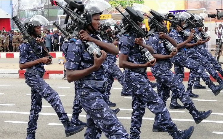 Des agents en uniforme bleu camouflage et casque transparent défilent en rang lors d'une cérémonie militaire