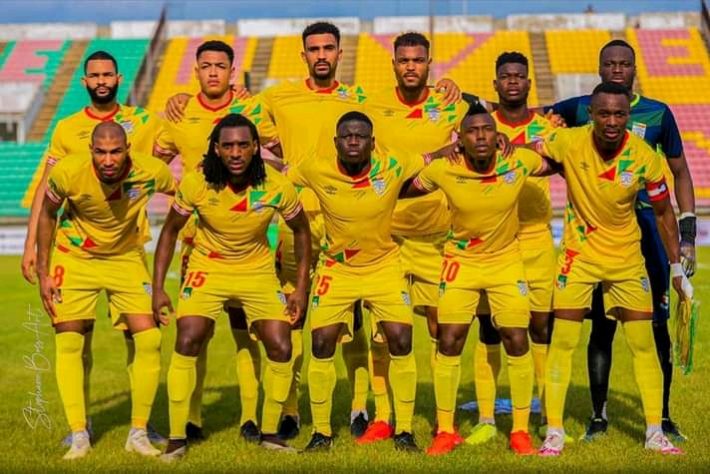 Onze joueurs en tenue jaune posant sur un terrain de football dans un stade aux gradins partiellement vides