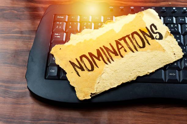 Carte déchirée avec le mot nominations posée sur un clavier d'ordinateur noir sur fond bois
