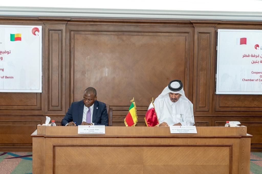 Deux hommes assis à une table signent des documents avec des drapeaux sur la table dans une salle de réunion formelle