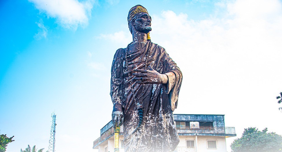 Statue d’un personnage historique en bronze sous un ciel bleu avec un bâtiment en arrière-plan