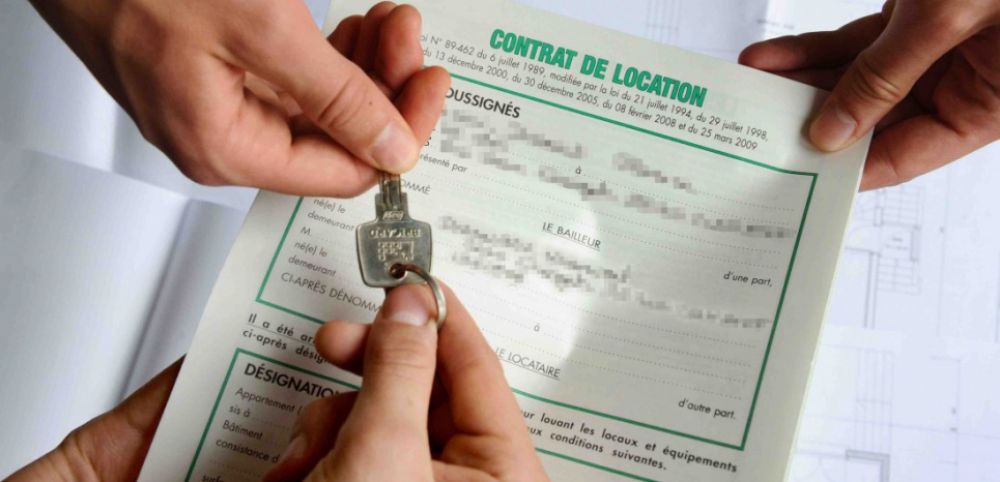 Une personne tient un trousseau de clés au-dessus d’un contrat de location posé sur une table