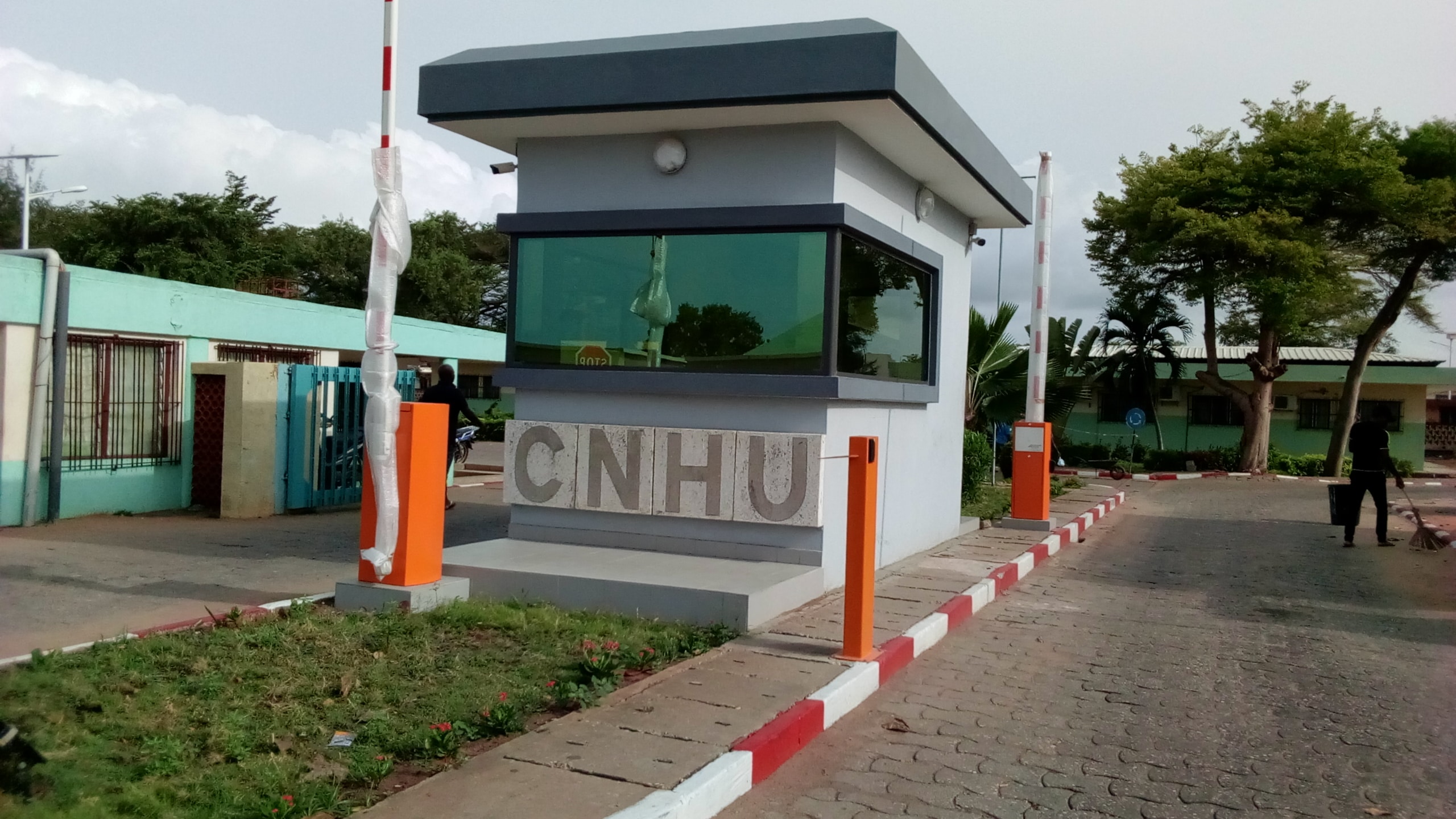Entrée sécurisée avec un poste de garde et un panneau affichant les lettres CNHU sur une chaussée bordée de pelouse et d’arbres