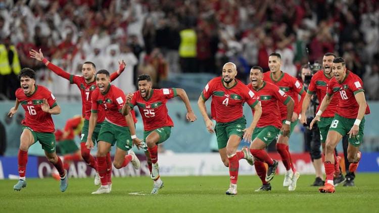 Une équipe de football en tenue rouge et verte court en célébrant sur un terrain devant un public nombreux