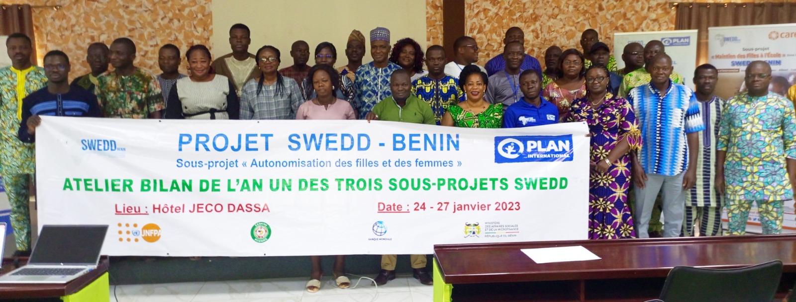 Un groupe de personnes posant derrière une grande banderole annonçant un atelier bilan du projet SWEDD-Bénin à l'hôtel JECO DASSA en janvier 2023
