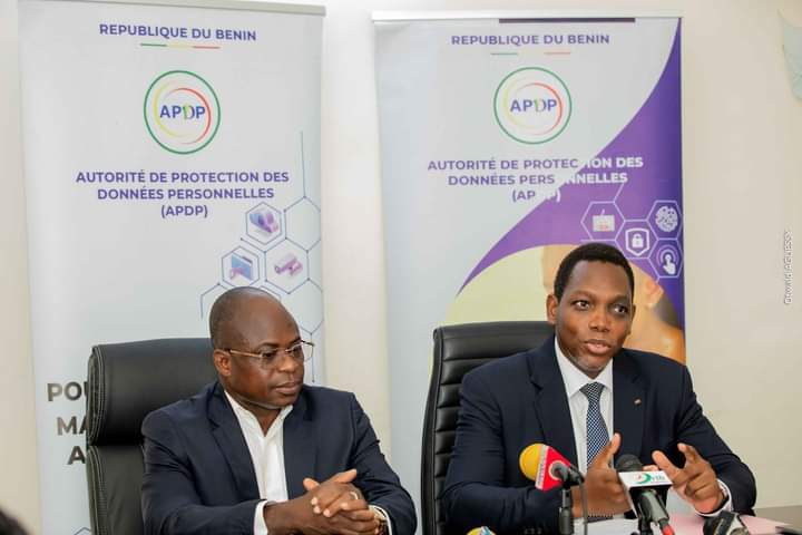 Deux hommes en costume parlent lors d’une conférence avec des panneaux officiels sur la protection des données personnelles en arrière-plan