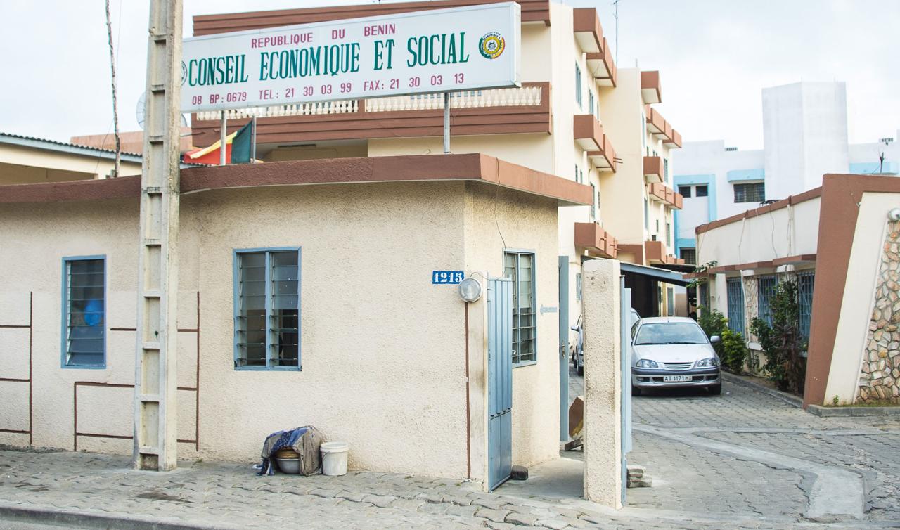Entrée d'un bâtiment administratif avec un panneau « Conseil économique et social » et une voiture stationnée sur un chemin adjacent