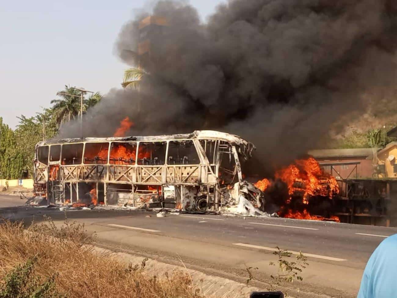 Autobus entièrement calciné en flammes et fumée noire dense sur une route asphaltée en milieu ouvert