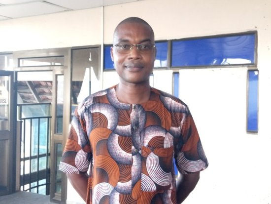 Homme portant une chemise à motifs colorés et des lunettes se tient debout dans un bâtiment lumineux