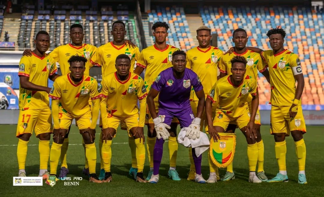 Onze joueurs de football en tenue jaune posent sur un terrain vide dans un grand stade assis en arrière-plan