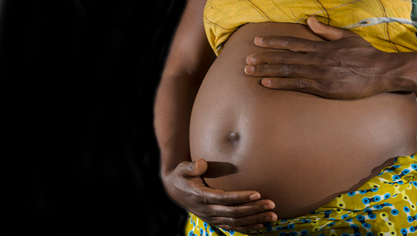Mains d’une femme enceinte posées sur son ventre arrondi vêtu d’un pagne jaune à motifs bleus et verts sur fond noir